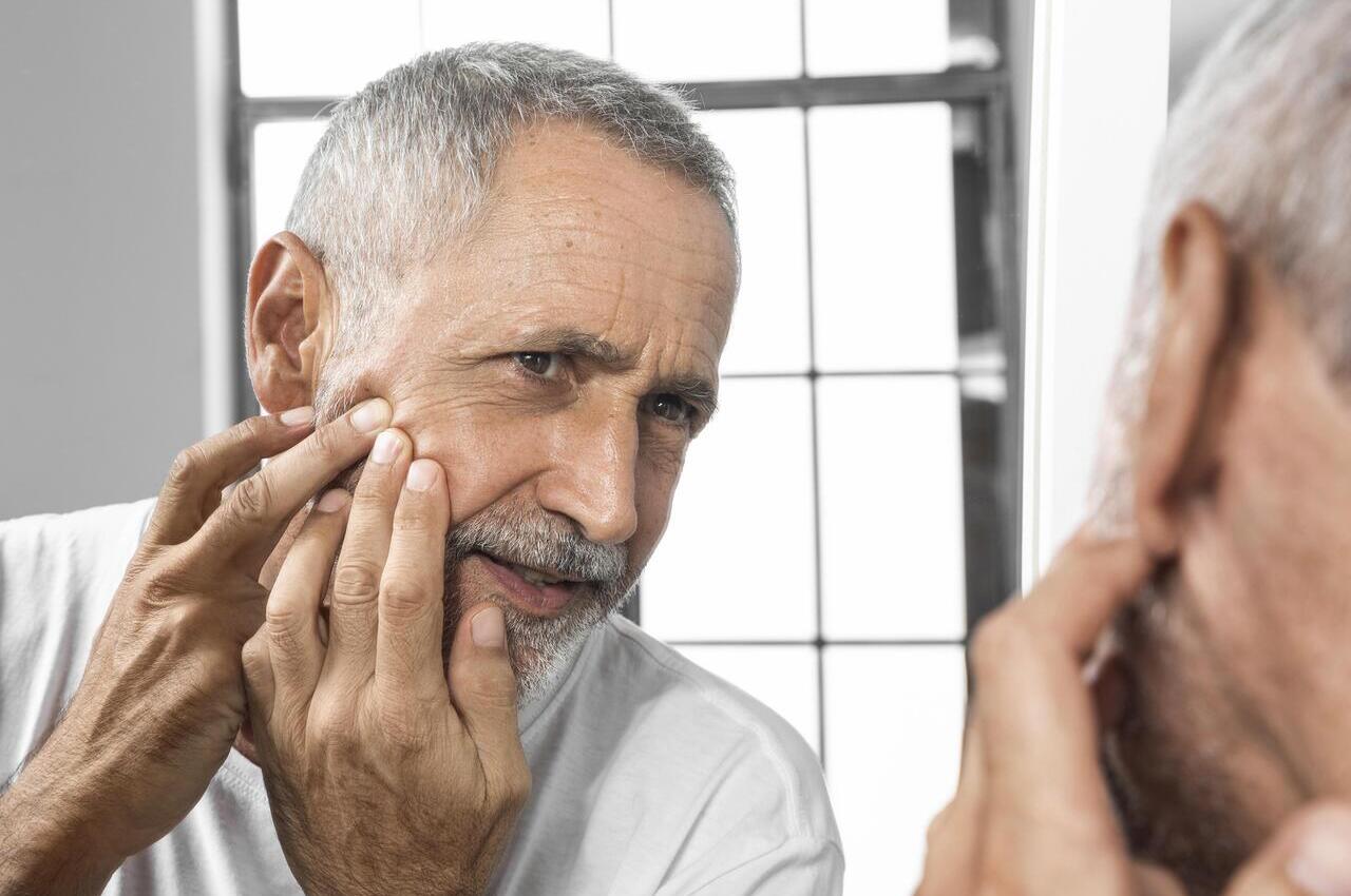 Adulto mayor observando su piel frente a un espejo