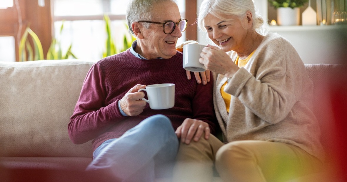 Dos personas mayores, que disfrutan de un envejecimiento saludable, desayunando un café y sonriendo