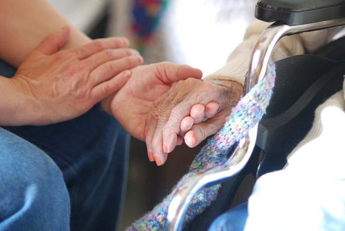 Adulto dando la mano a una anciana en silla de ruedas que no se puede mover