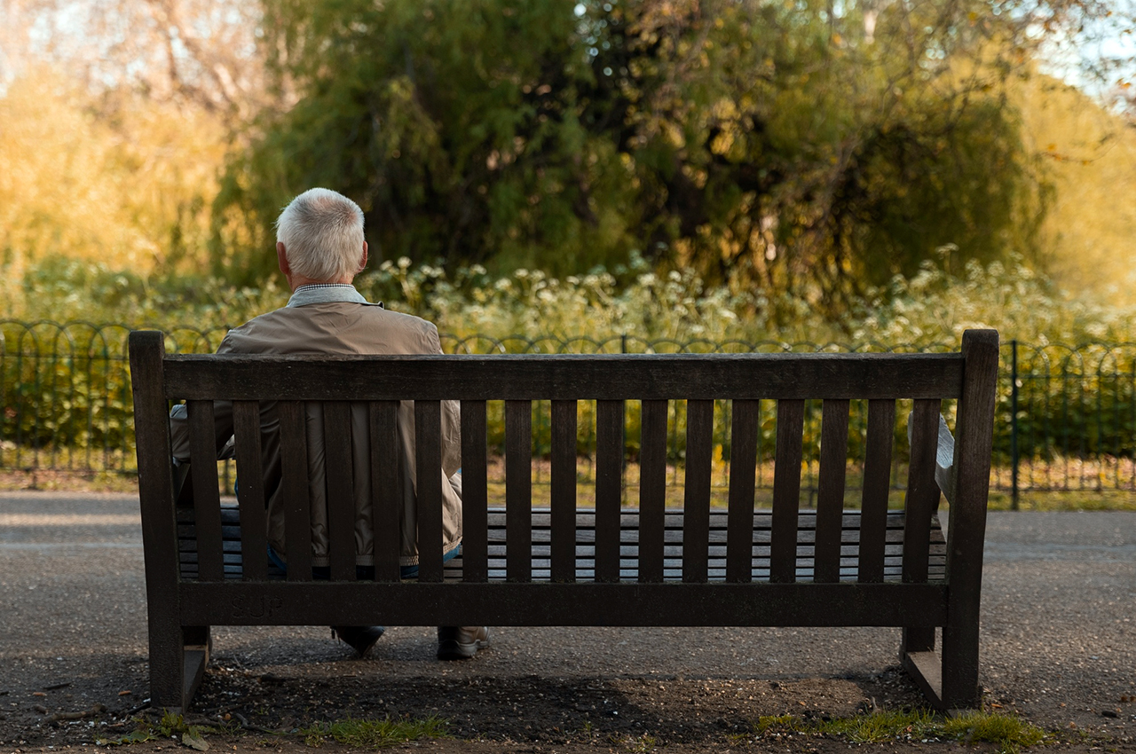 Anciano sentado de espaldas en el banco de un parque