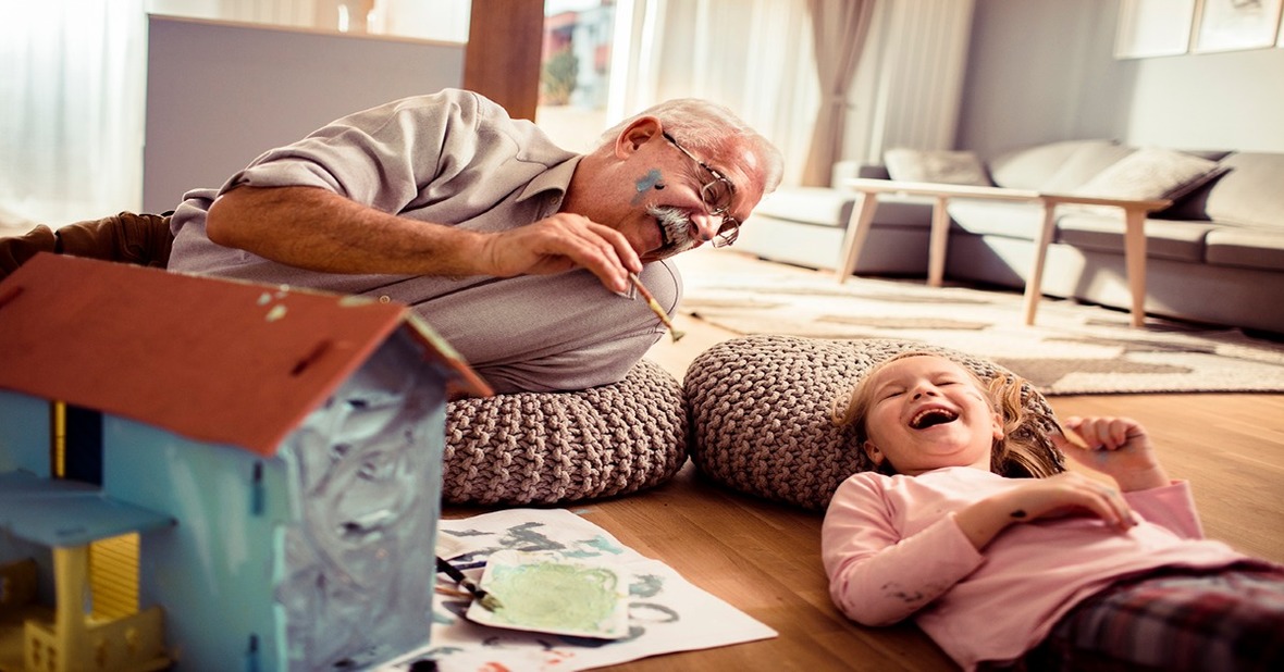 Nieta y abuelo en casa pintando una maqueta mientras se ríen y se manchan de pintura la cara