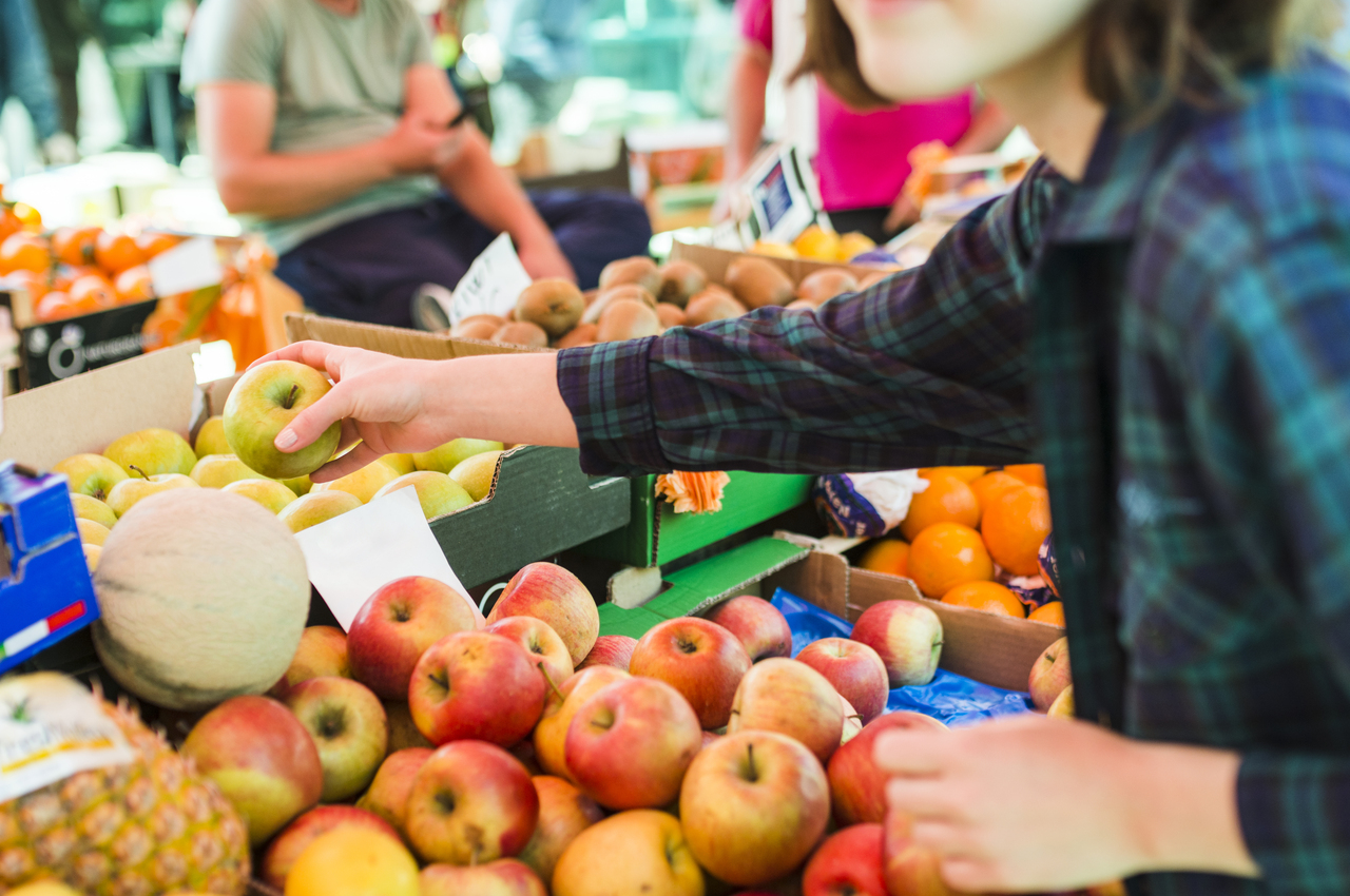 Una mujer joven escogiendo fruta en un mercado.