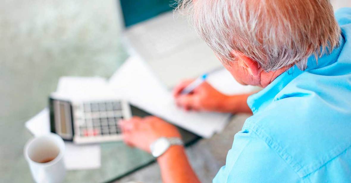 Hombre mayor rellenando papeles con una calculadora al lado para solicitar la pensión de viudedad