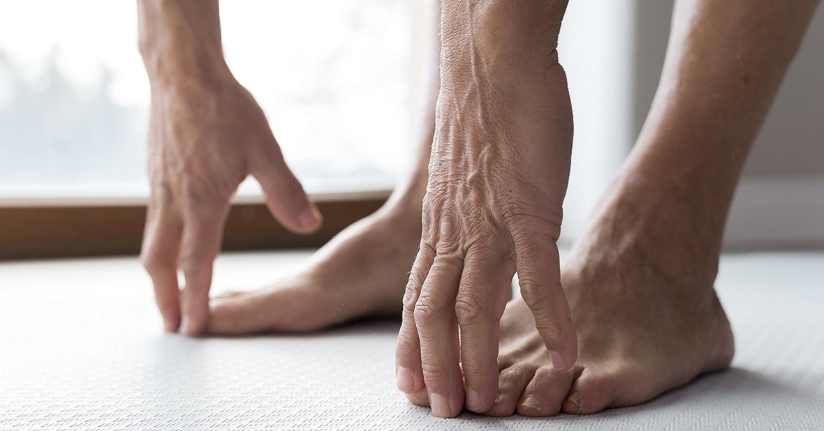 Persona mayor tocando la pinta de sus pies con los dedos de las manos, un ejercicio de estiramiento recomendable si sufrimos dolores en las piernas