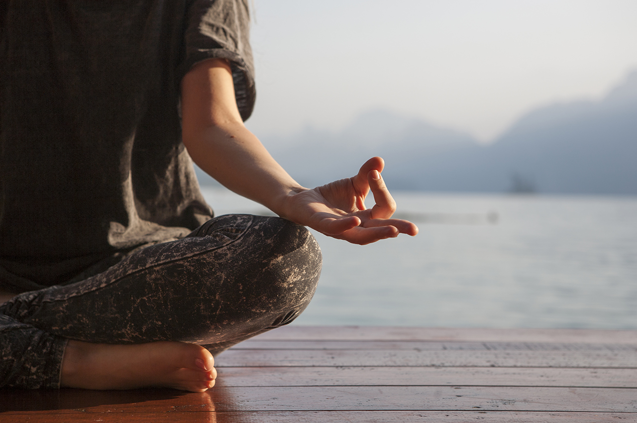 Una persona practica meditación sentada en un muelle, observando al mar.