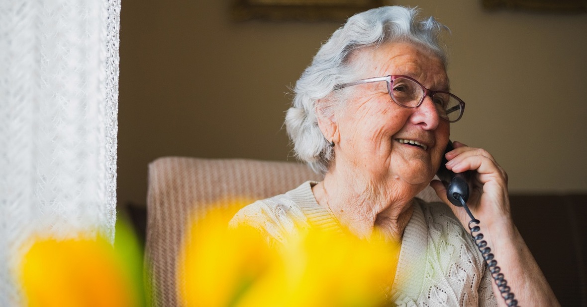 Persona mayor hablando por teléfono en el sofá de su casa para no sentirse sola, una forma de cuidar la salud mental