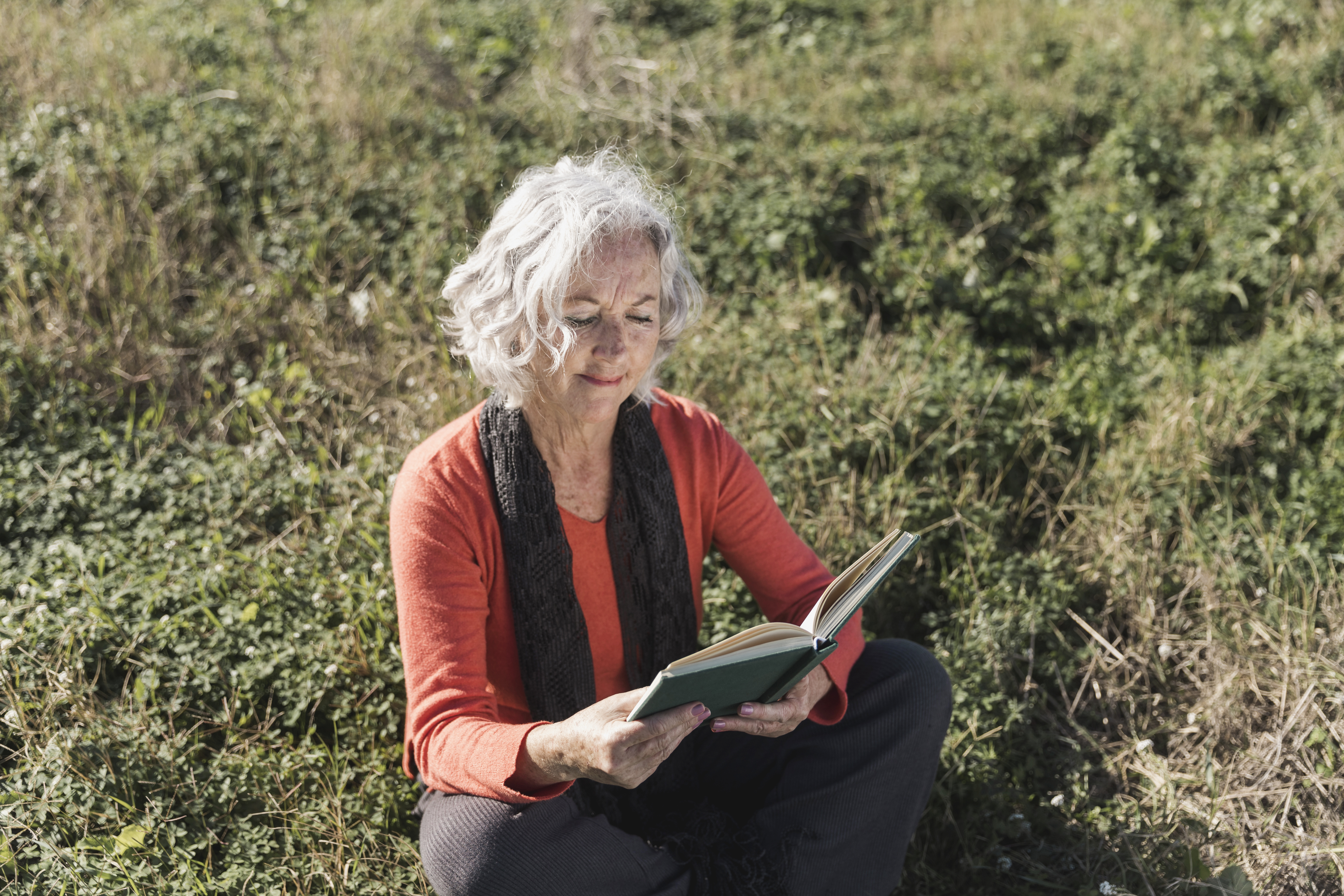 Una mujer mayor lee un libro en el césped.