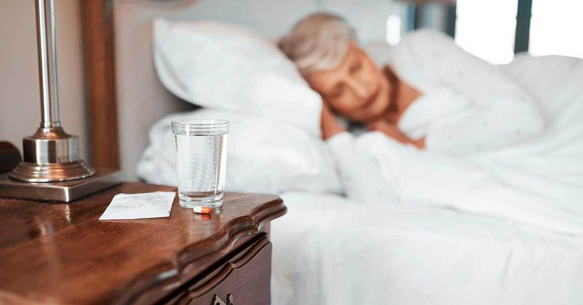 Mujer mayor durmiendo con un vaso de agua y pastillas en la mesilla para bajar la fiebre