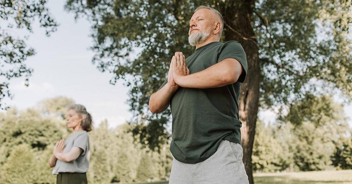 Pareja de personas mayores practicando yoga en un parque