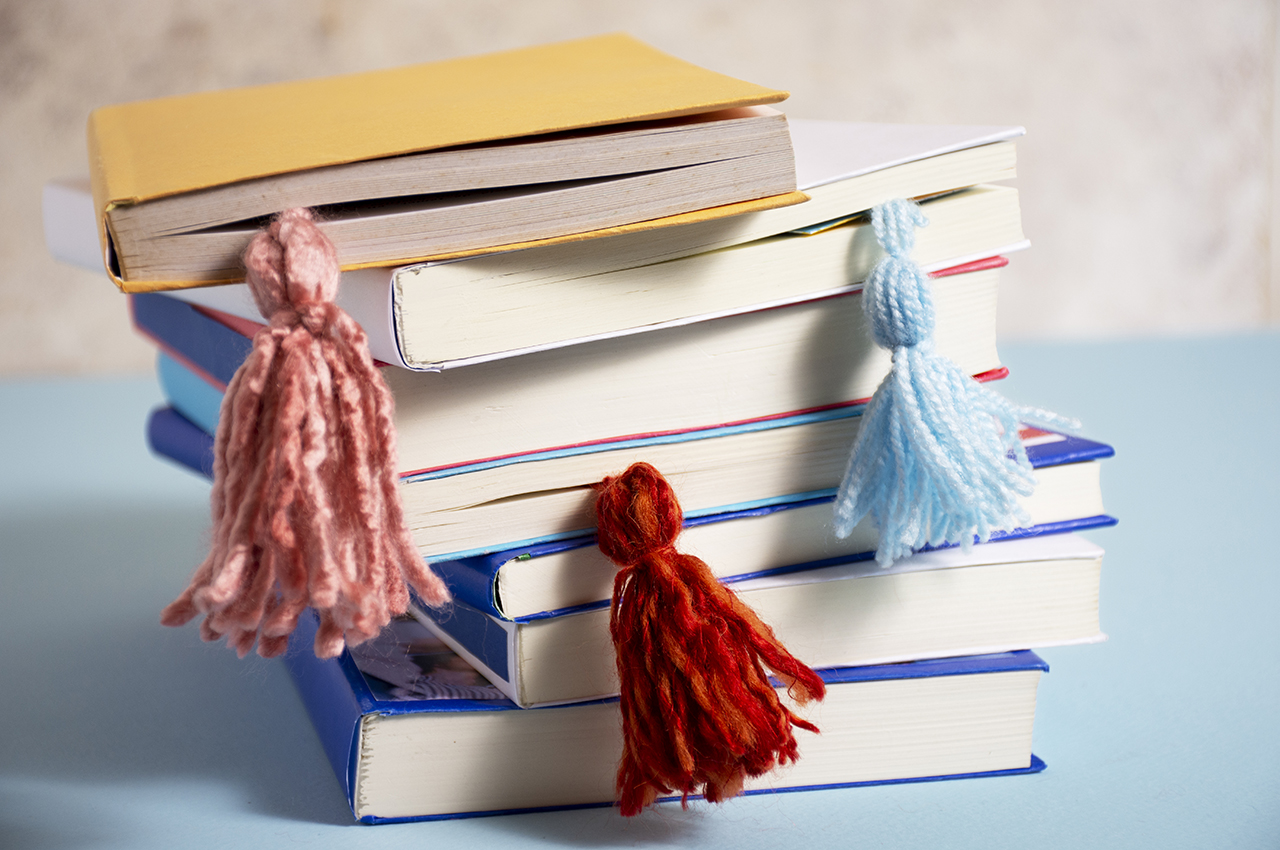 Una pila de siete libros con varios marcapáginas hechos con borlas de lana.