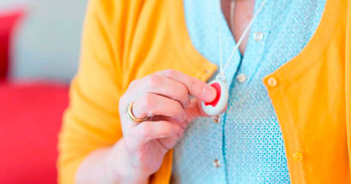 Mujer mayor pulsando el botón de teleasistencia que lleva con un colgante en el cuello