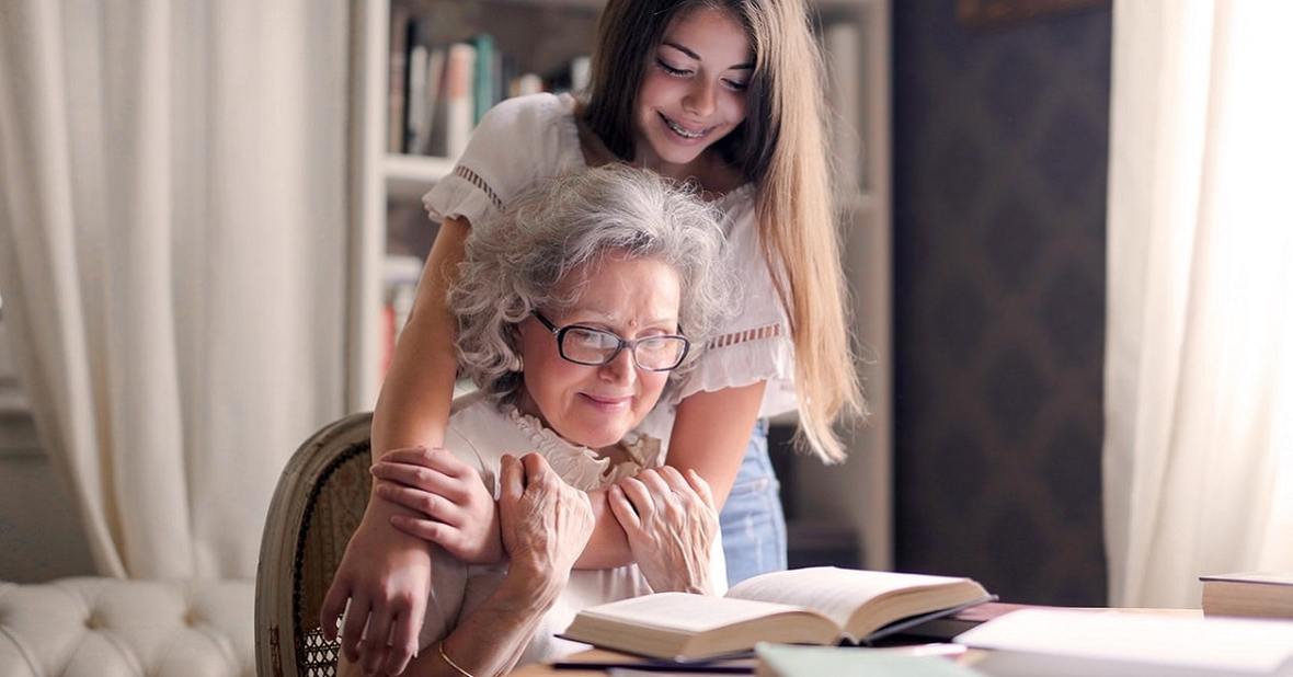 Nieta abrazando a su abuela, mientras la mujer mayor lee un libro