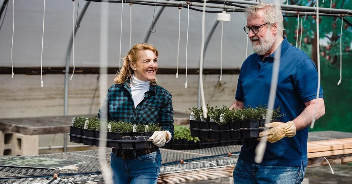 Dos personas mayores llevando varias plantas para hacer jardinería, otra forma de entrenar la psicomotricidad