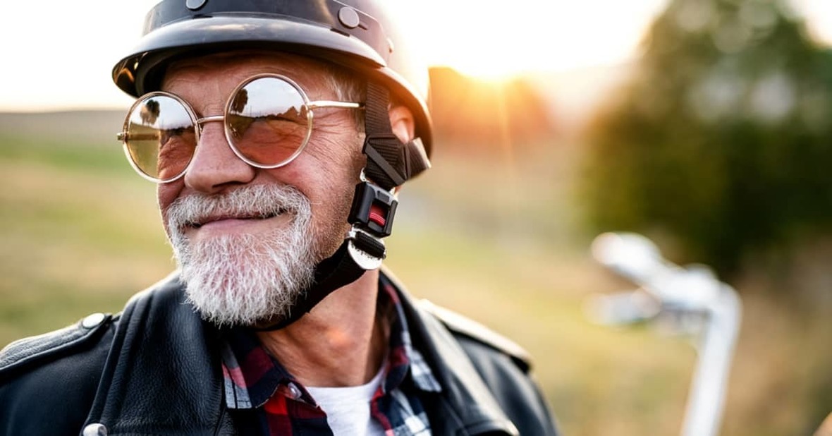 Hombre mayor sonriendo, vestido con una cazadora de cuero, un casco de moto y unas gafas de sol