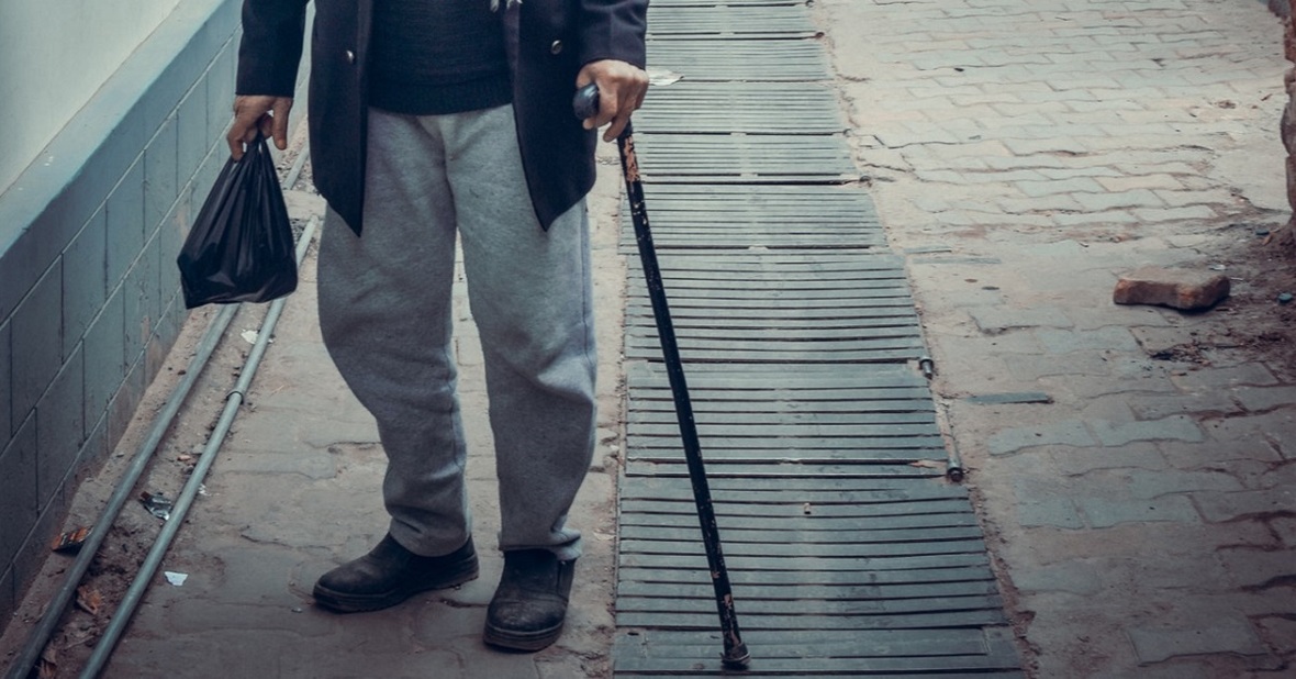 Hombre mayor con problemas de movilidad caminando por la calle con un bastón