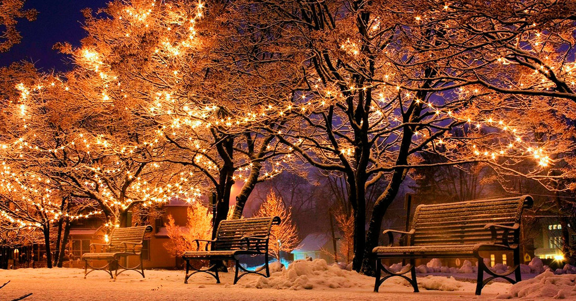 Estampa navideña de un parque nevado con árboles decorados con luces y bancos con nadie sentado, representando la soledad de los mayores en Navidad