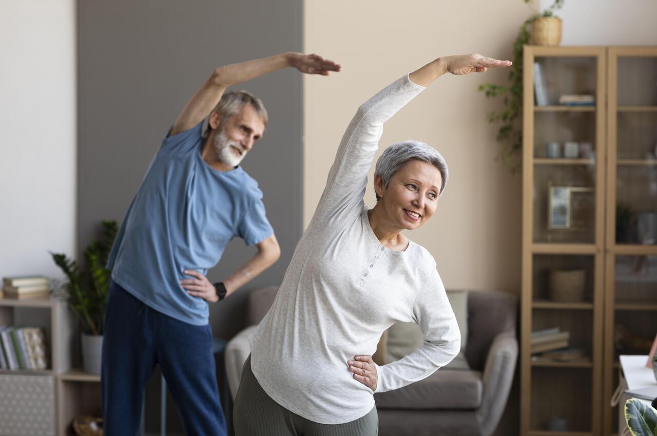 Dos personas mayores realizando estiramientos en su casa.