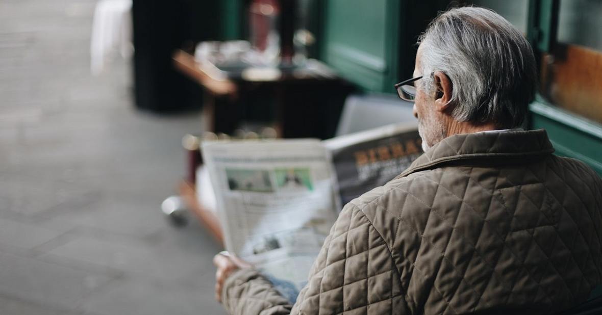 Hombre mayor leyendo el periódico sentado en la terraza de una cafetería