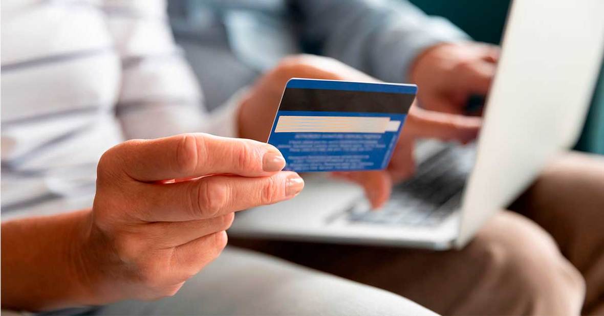 Persona mayor, que está siendo estafada, utilizando la tarjeta de crédito y el ordenador para pagar por internet